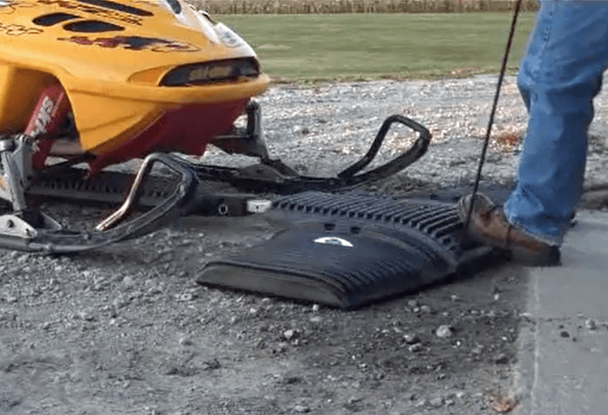 man pushing SledEZ under a snowmobile with his foot