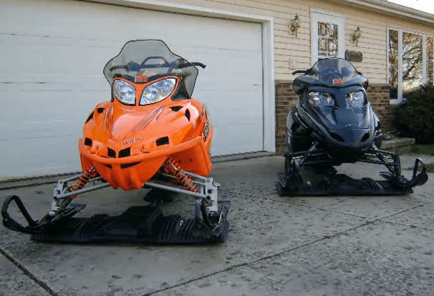 Two snowmobiles on SledEZ dollies outside a midwestern house