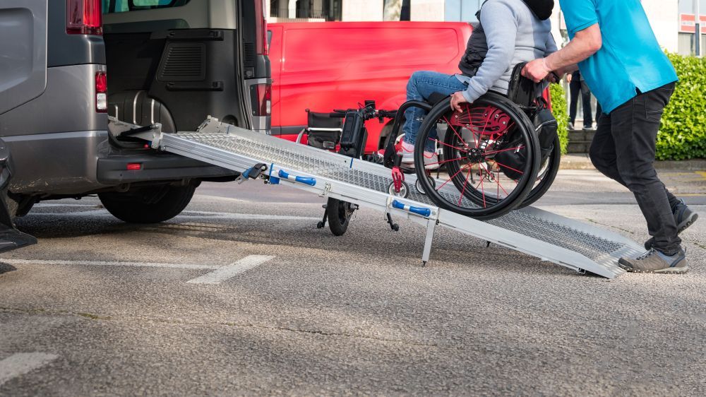 Photo of a person pushing another person in a wheelchair up a wheelchair van ramp.