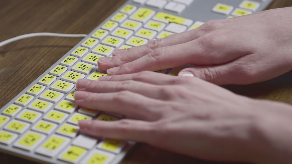 A close up of a person's hands as they use a braile keyboard
