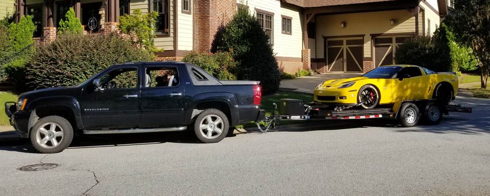 truck towing a yellow corvette on an open trailer in a neighborhood