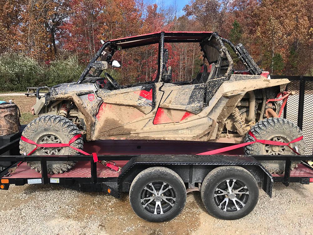 Muddy UTV tied down to an open trailer