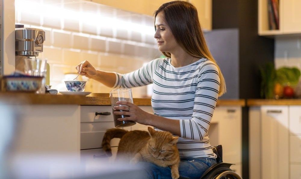 Photo of a person using a wheelchair making a cup on tea in the kitchen.