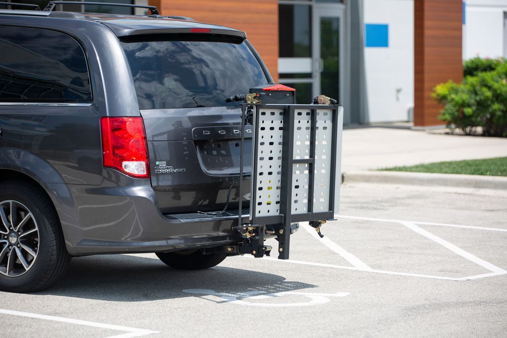gray minivan parked in disabled parking spot outside building with folded up hitch-mounted carrier