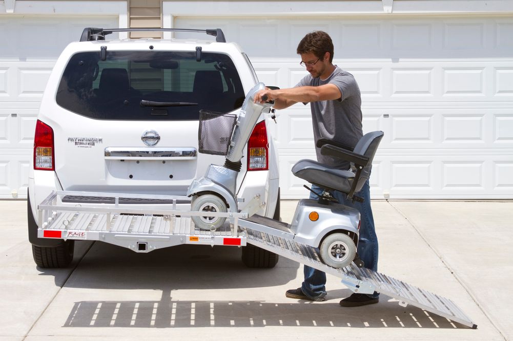 man moving a mobility scooter up onto a hitch-mounted carrier