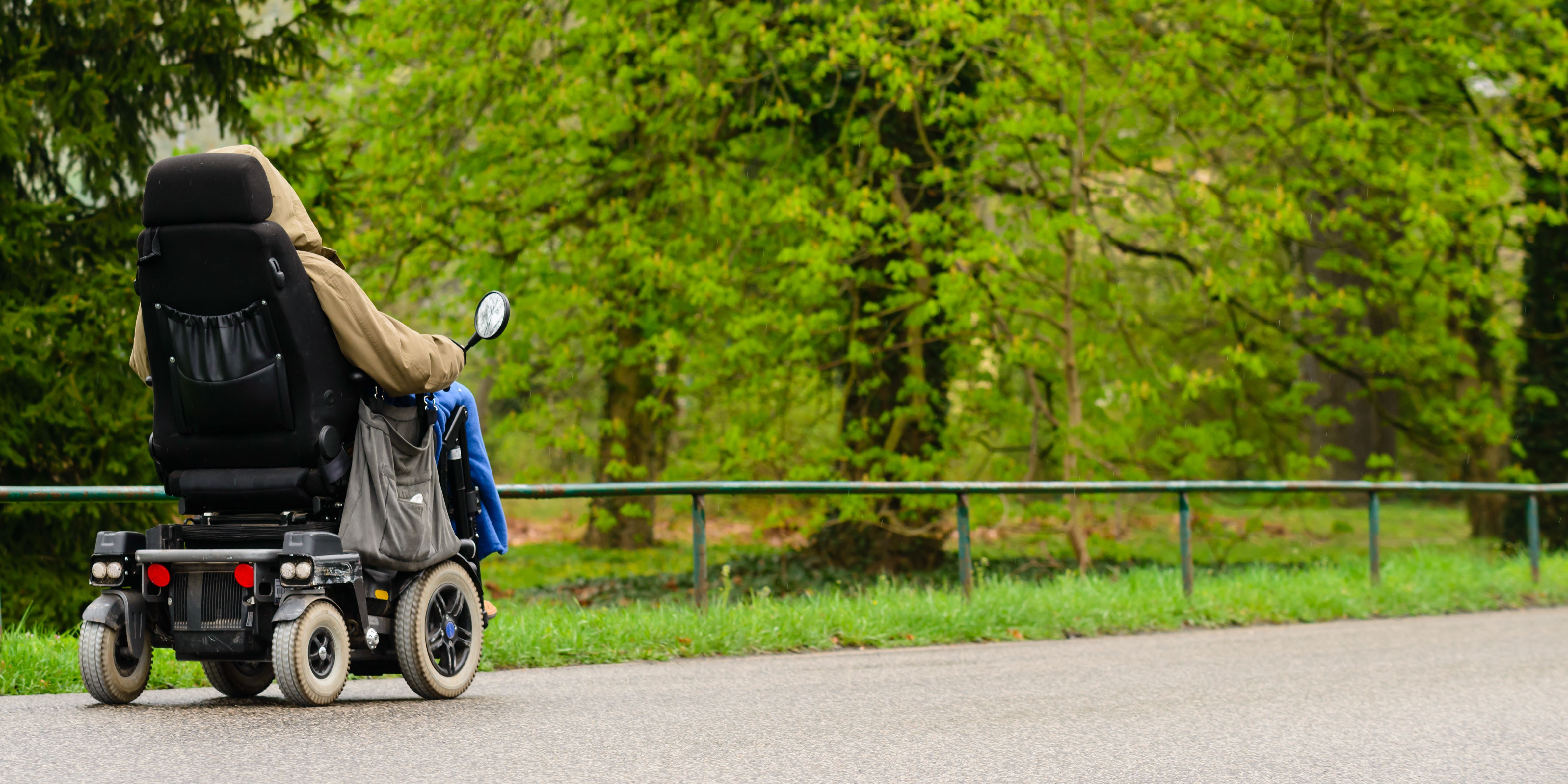 Person using a powerchair to ride down the road near a green forest