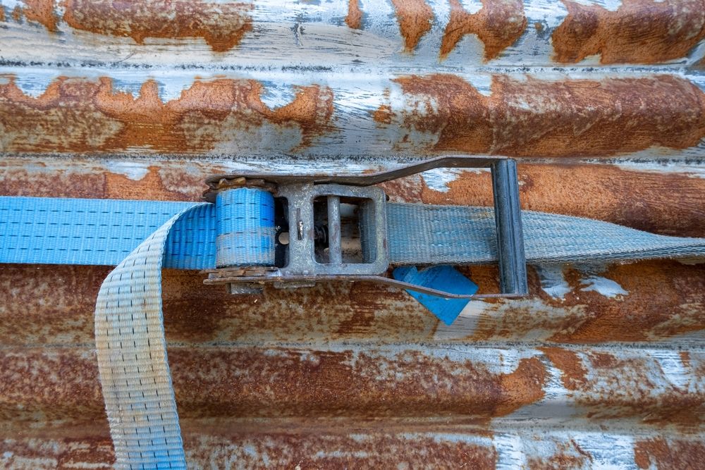 blue ratchet strap with rusty ratchet mechanism tighened around rusted corrugated iron sheet