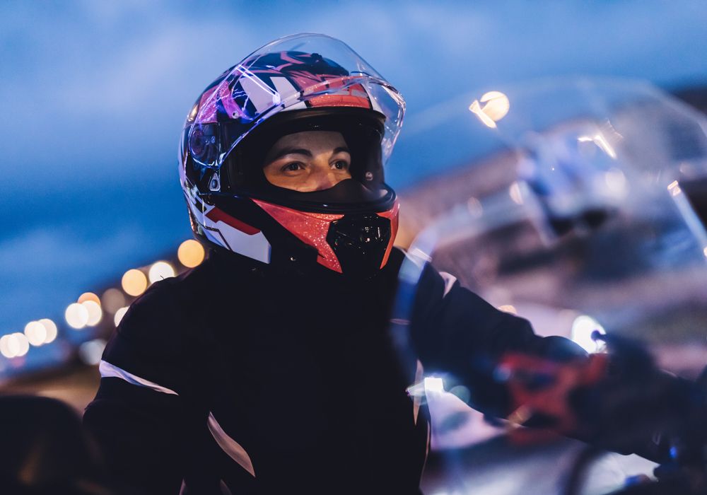 woman wearing a helment riding a motorcycle at night with city lights in the background