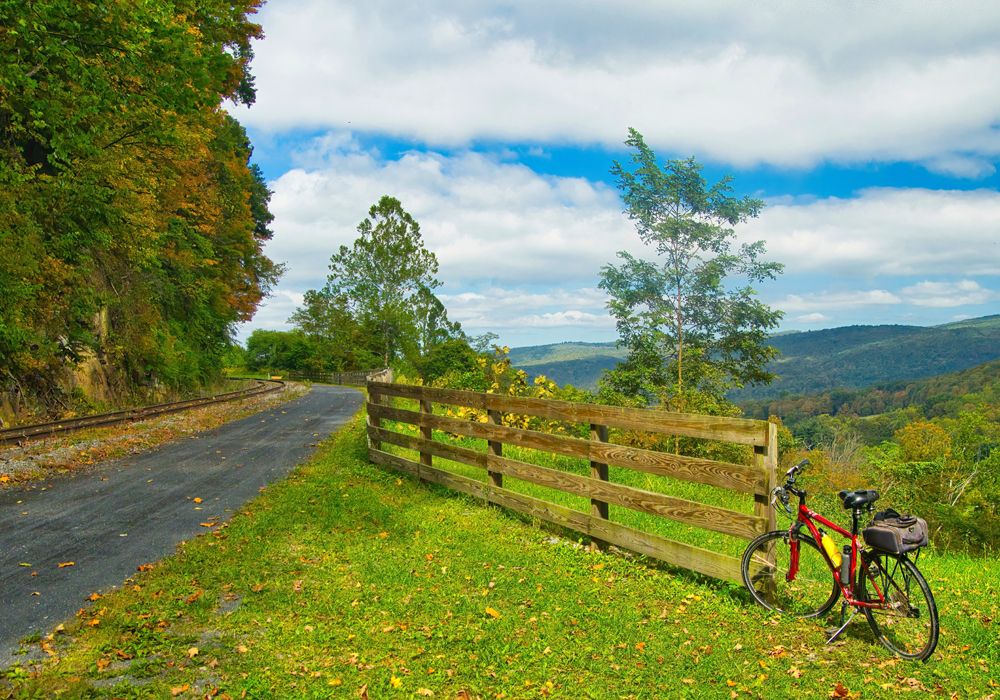 landscape of the Great Allegheny Passage trail featuring a bike alongside a fence in the mountains on an early Autumn day