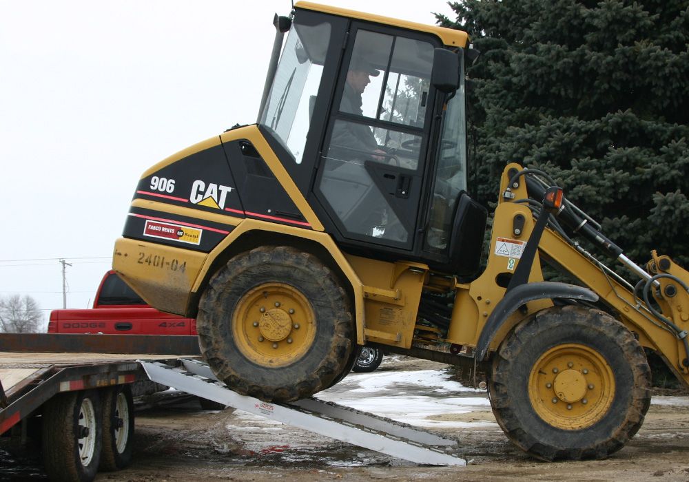 skid loader driving down a loading ramp onto the ground